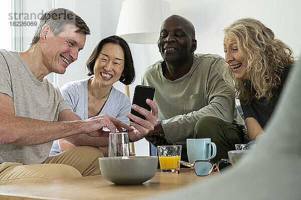 Mann mittleren Alters zeigt seiner Gruppe verschiedener Freunde drinnen ein Foto auf seinem Handy