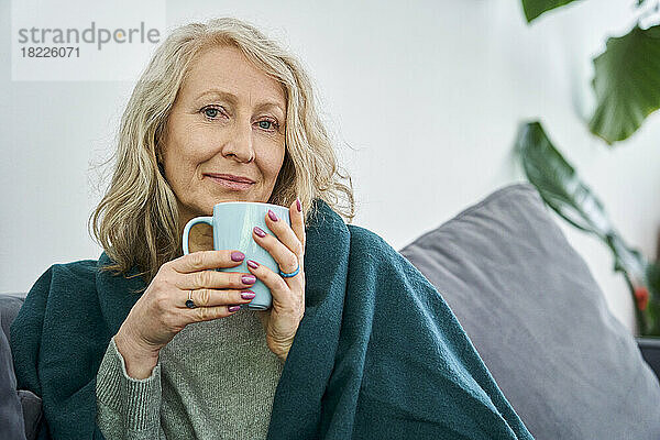 Ältere Frau trinkt eine Tasse Tee und schaut dabei in die Kamera