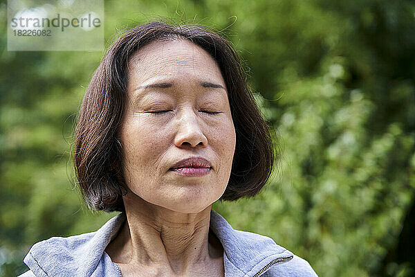 Ältere asiatische Frau mit geschlossenen Augen steht drinnen