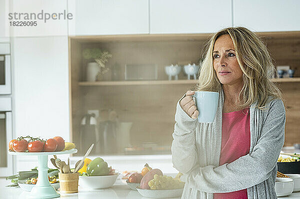 Porträt einer attraktiven Frau mittleren Alters mit einer Tasse Kaffee und Blick in die Kamera  die in der Küche steht