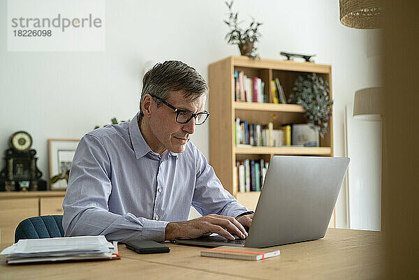 Leitender Geschäftsmann benutzt Laptop  während er zu Hause arbeitet