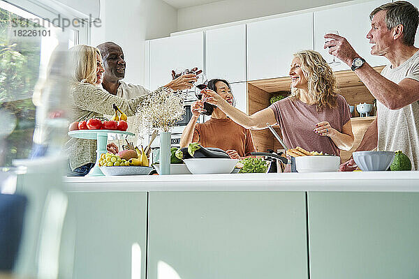 Eine vielfältige Gruppe älterer Freunde stößt an  während sie sich in der Küche versammelt
