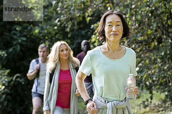 Senior Asian-American woman hiking in mountain trail with group of friends