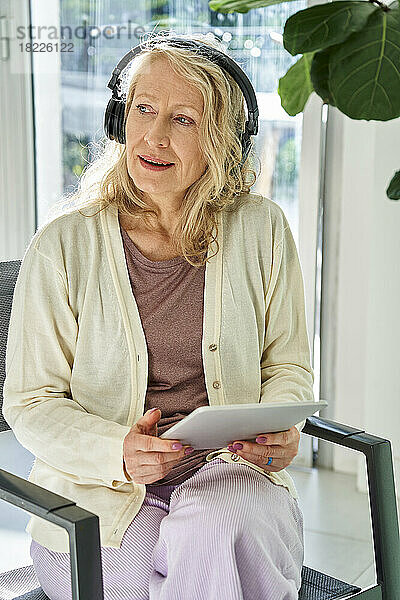 Ältere Frau hört Musik  während sie ein digitales Tablet verwendet
