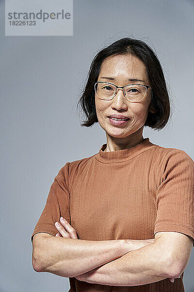 Reife asiatische Frau blickt mit verschränkten Armen in die Kamera