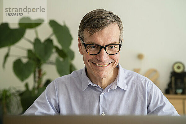 Älterer Mann lächelt  während er zu Hause Laptop benutzt