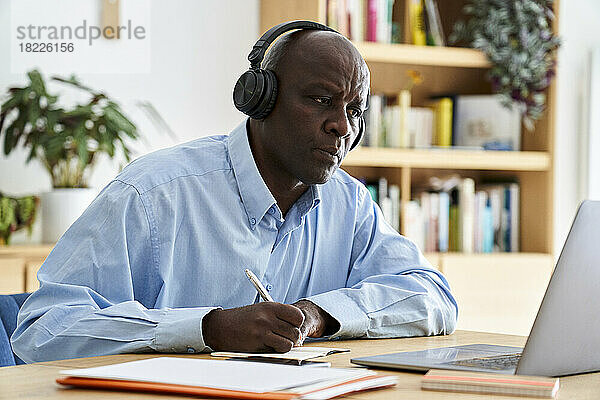 Reifer afroamerikanischer Mann trägt Kopfhörer  während er zu Hause mit einem Laptop arbeitet