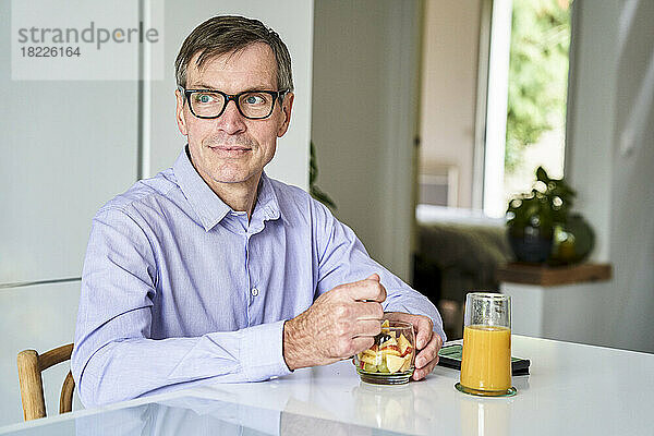 Berufstätiger Mann mittleren Alters frühstückt zu Hause auf der Küchentheke