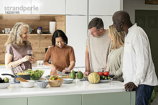 Eine Gruppe verschiedener Freunde mittleren Alters unterhält sich beim Kochen auf der Kücheninsel