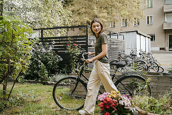 Seitenansicht einer jungen Frau  die mit dem Fahrrad fährt und Blumen im Garten betrachtet