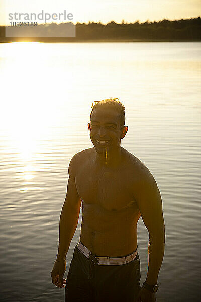 Glücklicher Mann ohne Hemd am See bei Sonnenuntergang