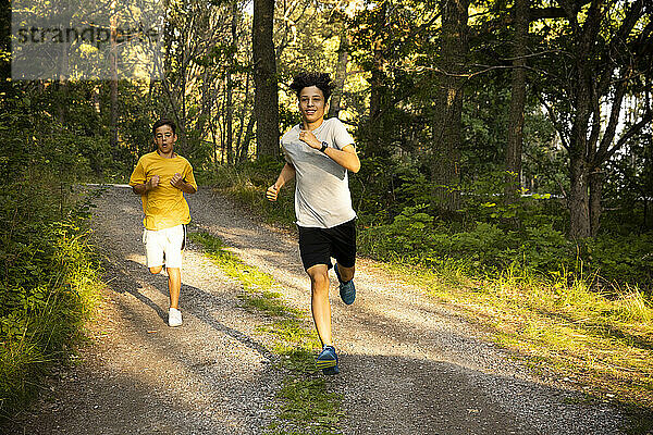 Aufgeregte Jungen  die in den Ferien gemeinsam auf einem unbefestigten Weg im Wald laufen