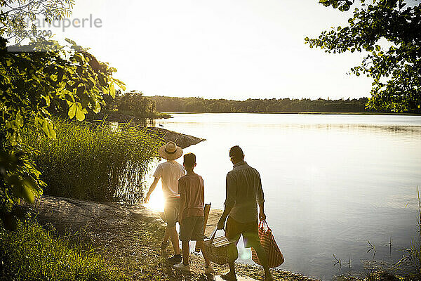 Familie mit Picknickausrüstung bei einem Spaziergang am Seeufer in den Sommerferien