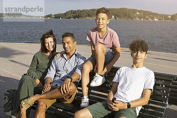 Porträt einer lächelnden Familie  die zusammen auf einer Bank am Meer sitzt
