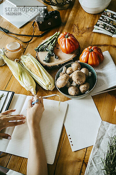 Hohe Winkel Ansicht der verschiedenen Gemüse mit Lebensmittel-Stylist Schreiben in Buch am Tisch