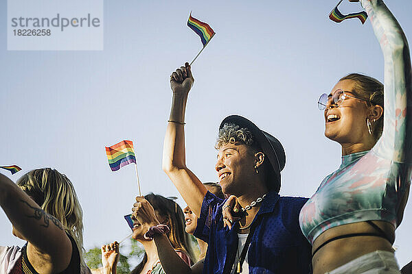 Glücklicher Mann und Frau mit erhobenen Händen  die Regenbogenfahnen halten  während sie an der Gay Pride Parade teilnehmen