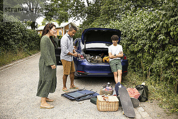 Familie diskutiert miteinander  während sie in der Nähe des Autos steht und sich Picknickzubehör ansieht