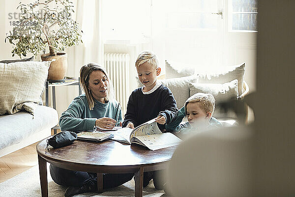 Mutter sitzt mit Söhnen bei den Hausaufgaben auf dem Tisch zu Hause