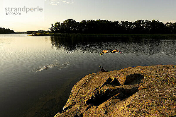 Mann beim Tauchen im See während des Urlaubs bei Sonnenuntergang