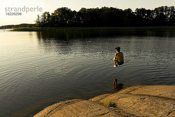 Junge springt im Urlaub bei Sonnenuntergang in den See