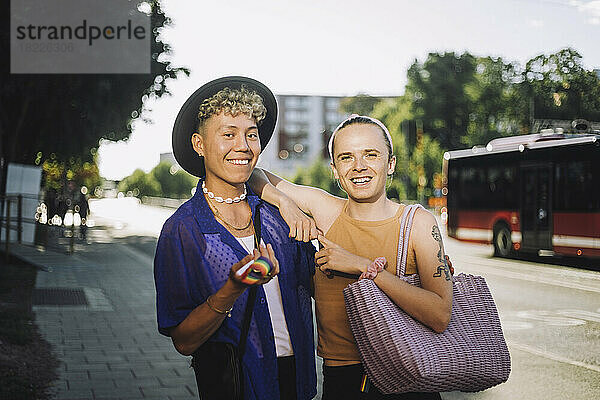 Porträt einer glücklichen nicht-binären Person  die neben einem jungen Mann mit Hut steht