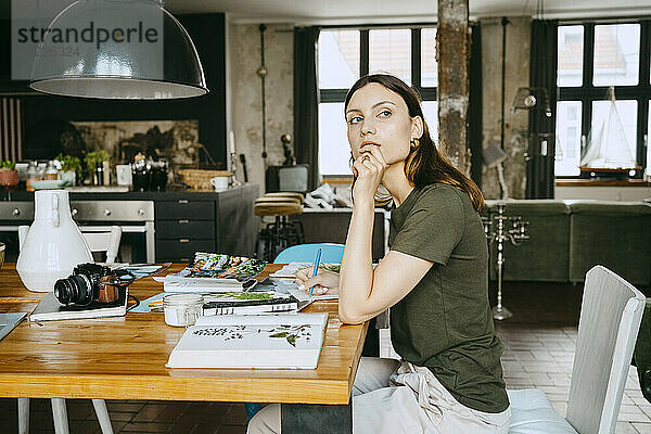 Weibliche Food-Stylistin mit Hand am Kinn  die wegschaut  während sie am Tisch im Studio sitzt