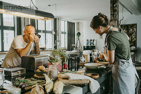 Fotograf  der ein Bild von einem Koch macht  der in einer Studioküche Essen zubereitet