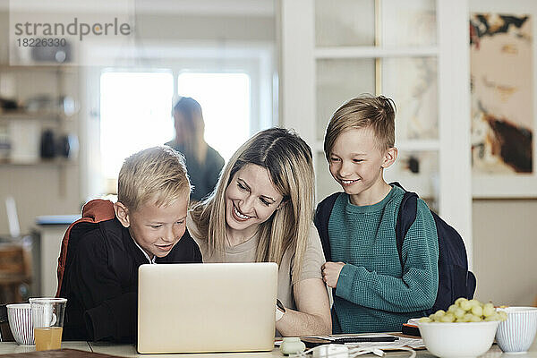 Glückliche Mutter mit aufgeregten Söhnen  die zu Hause auf den Laptop schauen