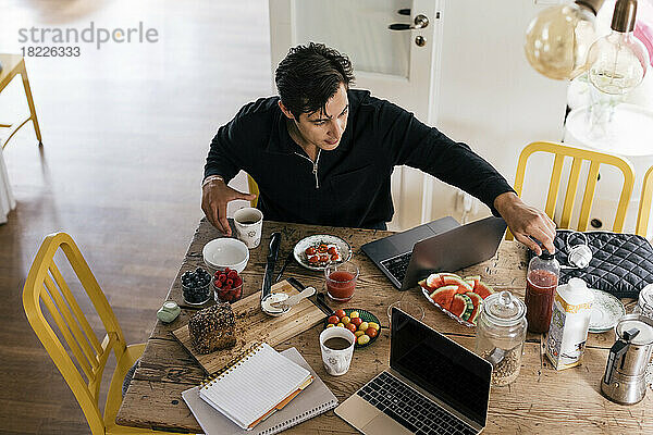 Hohe Winkel Ansicht der männlichen Freiberufler beim Frühstück  während mit Laptop auf Esstisch zu Hause sitzen