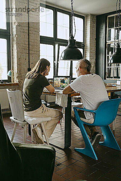 Männliche und weibliche Geschäftskollegen diskutieren über einen Laptop  während sie auf einem Stuhl im Studio sitzen