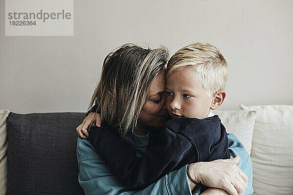 Mutter  die ihren Sohn umarmt  während sie zu Hause auf dem Sofa sitzt