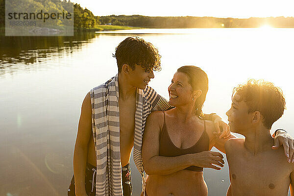 Glückliche Söhne im Gespräch mit ihrer Mutter  während sie bei Sonnenuntergang am See stehen
