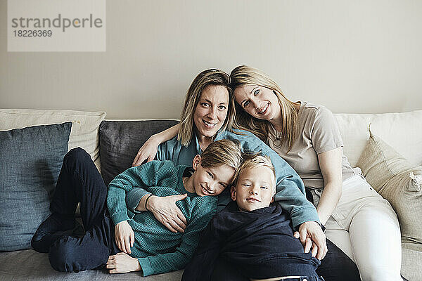 Porträt von lesbischen Müttern mit Söhnen  die zusammen auf dem Sofa zu Hause sitzen