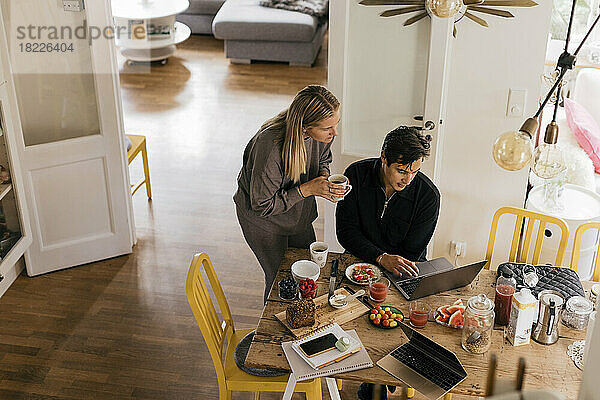 Männliche und weibliche Freiberufler  die beim Frühstück zu Hause am Laptop arbeiten