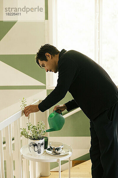 Seitenansicht eines jungen Mannes  der Pflanzen auf einem Beistelltisch zu Hause gießt