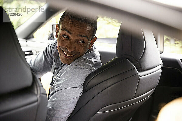 Glücklicher Mann schaut über die Schulter zurück  während er im Auto sitzt