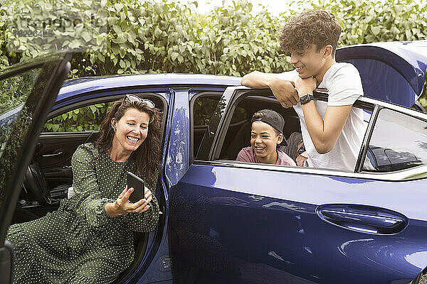 Aufgeregte Frau teilt ihr Smartphone mit ihren Söhnen  die im Auto sitzen