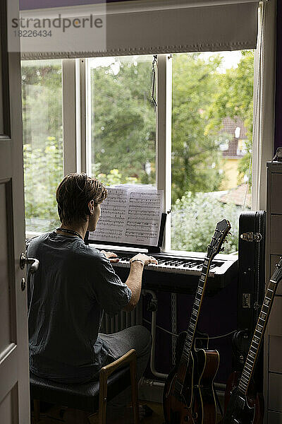 Rückansicht eines Mannes  der beim Klavierspielen zu Hause Noten liest