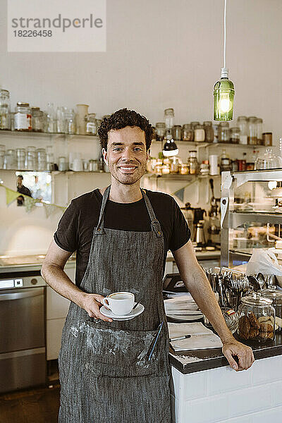 Lächelnder männlicher Besitzer mit Kaffeetasse in einem Café stehend