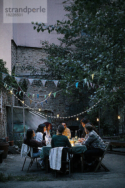 Eine Gruppe von Freunden genießt das Abendessen in einem dekorierten Hinterhof