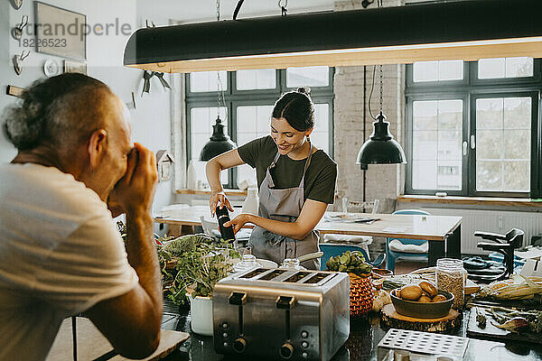 Lächelnde junge Köchin bei der Zubereitung von Speisen mit einem Fotografen  der ein Bild in einer Studioküche macht