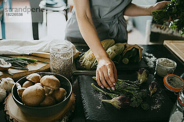 Köchin arrangiert Broccolini und Auberginen auf einer Schiefertafel in der Studioküche