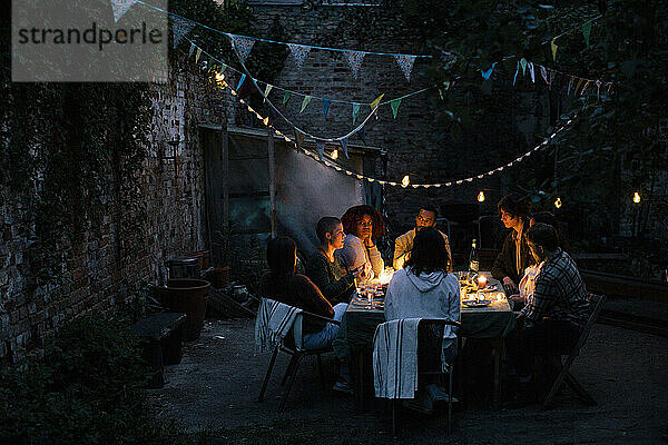 Multirassische Freunde bei einer Dinnerparty im beleuchteten Hinterhof