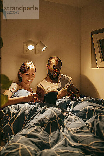 Mann und Frau lesen Bücher  während sie sich zu Hause auf einem Bett mit Decke ausruhen