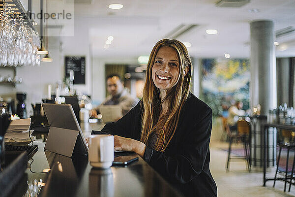 Porträt einer lächelnden weiblichen Fachkraft  die mit einem Laptop an der Theke eines Restaurants sitzt
