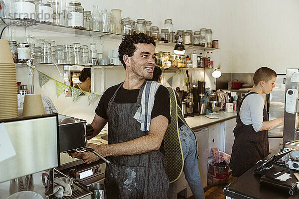 Lächelnder Besitzer schaut weg  während er in einem Café Kaffee zubereitet