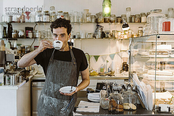 Männlicher Besitzer trinkt Kaffee  während er in der Nähe der Theke eines Cafés steht