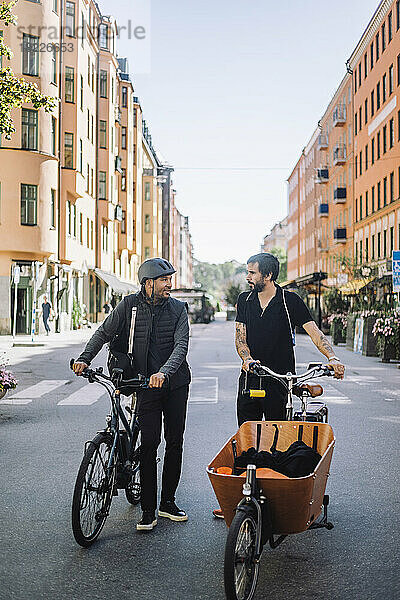 Männliche Geschäftskollegen mit Fahrrädern unterhalten sich im Stehen auf der Straße