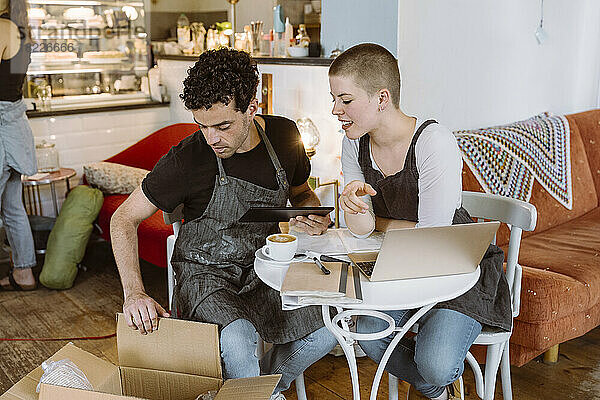 Männliche und weibliche Besitzer  die auf einem Stuhl in einem Café sitzen und eine Box überprüfen