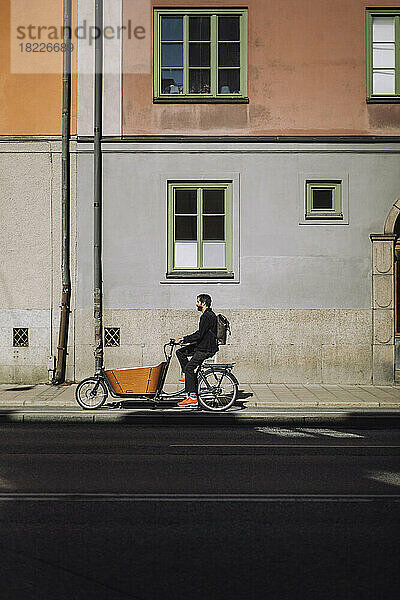 Geschäftsmann fährt Lastenrad gegen Gebäude an einem sonnigen Tag